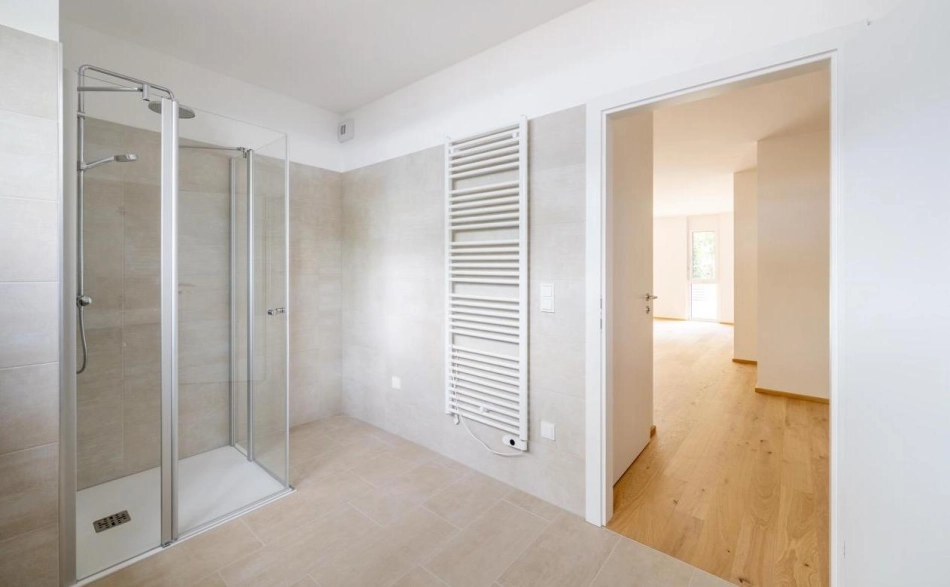 Badezimmer mit Dusche und Wandheizkörper mit Blick in einen anderen Raum, Wohnanlage Janzgasse.