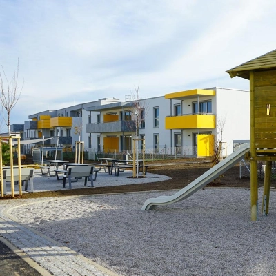 Außenansicht der Wohnanlage mit Balkonen, Spielplatz und Sitzgelegenheiten, Lachtengasse.