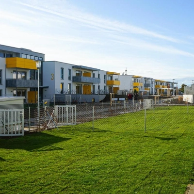 Außenansicht der Wohnanlage mit Balkonen, Zäunen und großer Grasfläche.